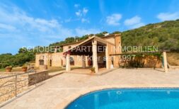 Finca in Son Carrió mit Pool, überdachter Terrasse und Natursteinmauern, eingebettet in grüne Hügellandschaft.