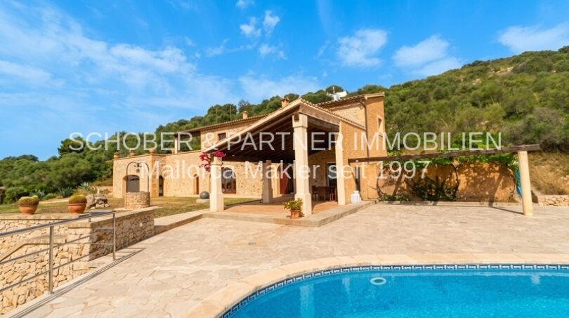 Finca in Son Carrió mit Pool, überdachter Terrasse und Natursteinmauern, eingebettet in grüne Hügellandschaft.