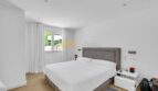 Helles Schlafzimmer der modernen Villa in Santa Ponça mit Doppelbett, Holzboden und weißen Wänden.