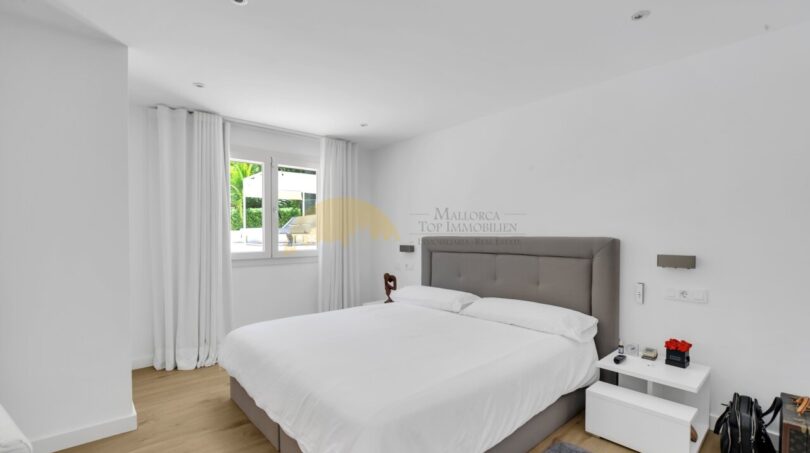 Helles Schlafzimmer der modernen Villa in Santa Ponça mit Doppelbett, Holzboden und weißen Wänden.
