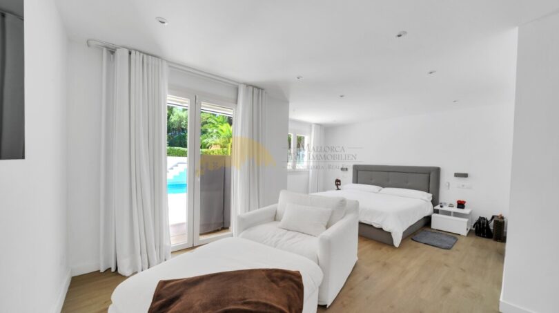 Helles Schlafzimmer der Villa in Santa Ponça mit Holzboden, Doppelbett und Poolblick durch Terrassentür.