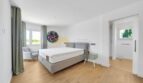 Helles Schlafzimmer der Villa in Santa Ponça mit Doppelbett, Holzboden und Zugang zum Bad.