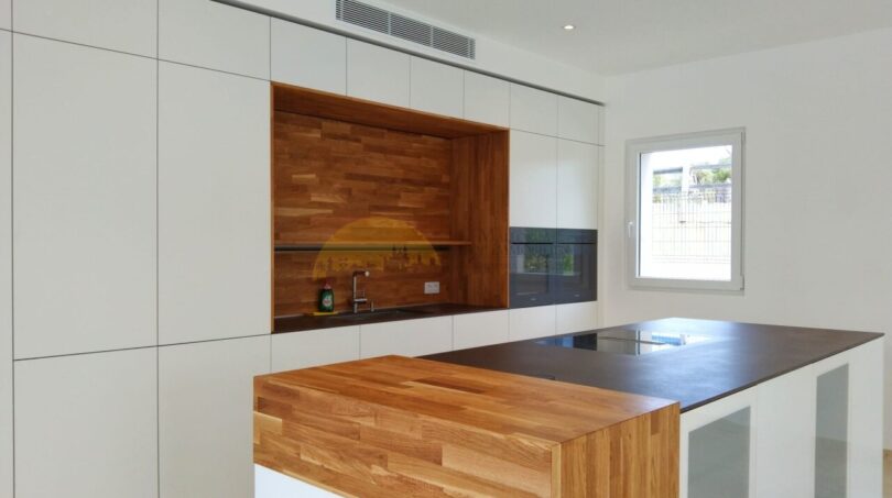 Moderne Einbauküche der Neubau Villa in Sol de Mallorca mit Kücheninsel und Holzakzenten