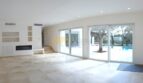 Helles Wohnzimmer der Neubau Villa Sol de Mallorca mit Kamin, Marmorboden und Blick auf Pool und Olivenbaum