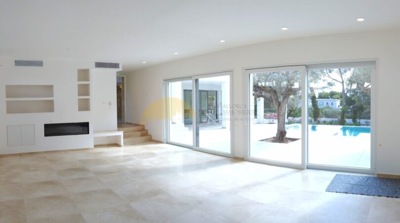Helles Wohnzimmer der Neubau Villa Sol de Mallorca mit Kamin, Marmorboden und Blick auf Pool und Olivenbaum