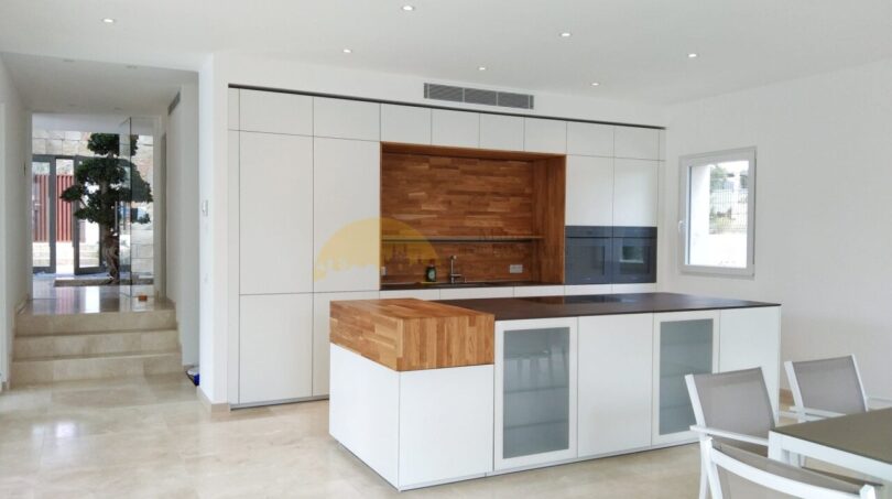 Moderne Einbauküche mit weißen Fronten, Holzakzenten und Kücheninsel in Neubau-Villa Sol de Mallorca