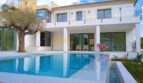 Neubau Villa Sol de Mallorca: Poolbereich mit blauem Wasser, weißer Fassade, Balkon und Olivenbaum