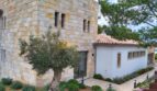 Außenansicht Neubau Villa Sol de Mallorca: Natursteinwände, weißer Anbau mit Terrakottadach, Olivenbaum und mediterraner Bepflanzung.