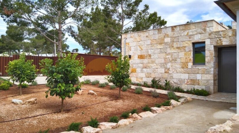 Einfahrt einer Neubau-Villa in Sol de Mallorca mit Natursteinmauer, mediterranem Garten und Pinien