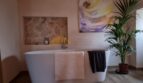 Elegantes Badezimmer der Finca in Felanitx mit freistehender Badewanne, Natursteinwand und Kunstwerk.