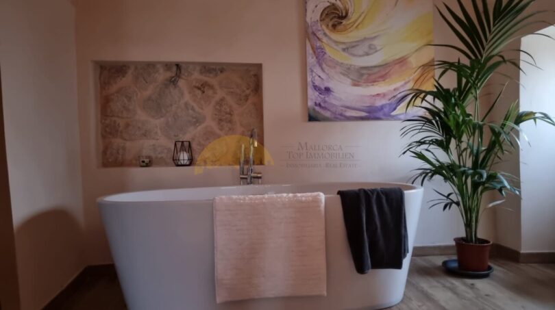 Elegantes Badezimmer der Finca in Felanitx mit freistehender Badewanne, Natursteinwand und Kunstwerk.