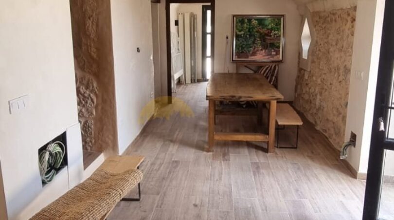 Weitläufiger Gewölbegang der Finca in Felanitx mit Holzboden, Natursteinwänden und rustikalem Holztisch.