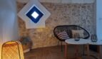 Gemütlicher Wohnbereich der Finca in Felanitx mit Steinwand, Rattanstuhl, Bambuslampe und rautenförmigem Fenster.