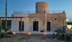 Finca Felanitx: Steinhaus mit rundem Turm, Dachterrasse, beleuchtetem Eingangsbereich und Pergola im Abendlicht.