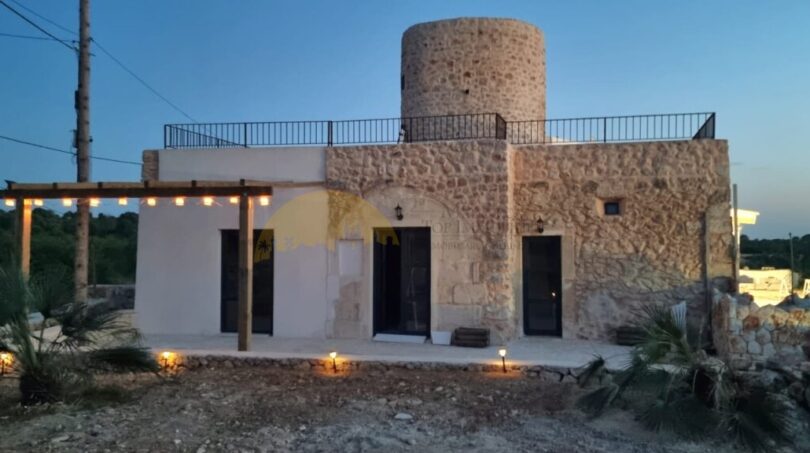 Finca Felanitx: Steinhaus mit rundem Turm, Dachterrasse, beleuchtetem Eingangsbereich und Pergola im Abendlicht.