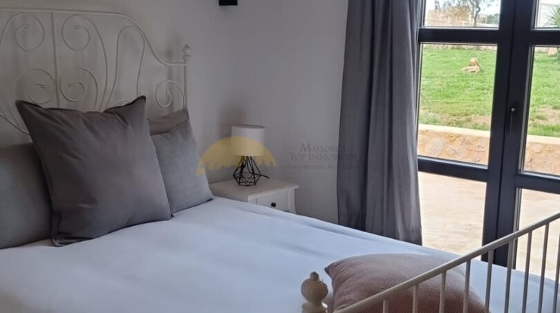 Schlafzimmer der Finca Felanitx mit Gewölbedecke, weißem Eisenbett und Zugang zum Garten