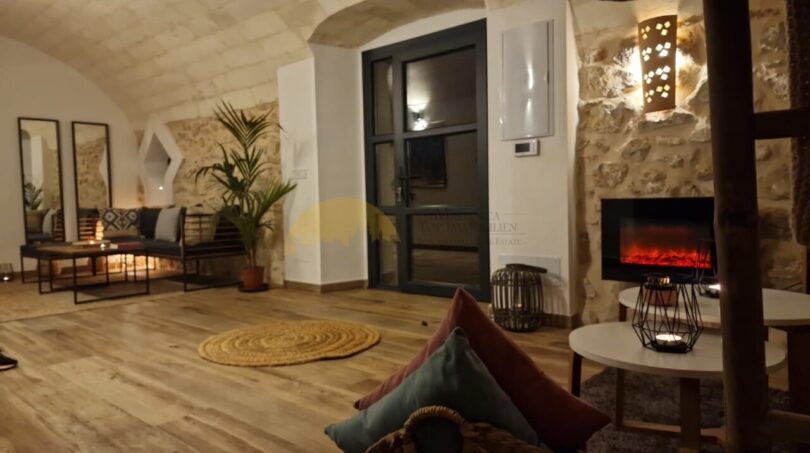 Gemütliches Wohnzimmer der Finca in Felanitx mit Natursteinwänden, Gewölbedecke, Holzboden und modernem Elektrokamin.