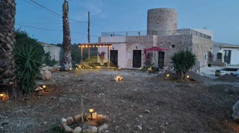 Beleuchteter Außenbereich der Finca in Felanitx bei Dämmerung mit Steinturm, Palmen und mediterranem Garten.