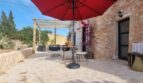 Sonnige Steinterrasse der Finca Felanitx mit rotem Sonnenschirm, Pergola und Bougainvillea