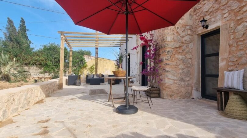 Sonnige Steinterrasse der Finca Felanitx mit rotem Sonnenschirm, Pergola und Bougainvillea