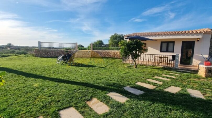 Gepflegter Garten der Finca in Felanitx mit Steinweg, Terrasse und mediterranem Bungalow unter blauem Himmel.