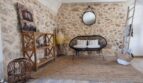 Rustikaler Wohnbereich der Finca Felanitx mit Natursteinwand, Rattansofa, Holzregal und dekorativen Elementen.