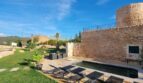 Finca Felanitx: Rustikaler Steinturm mit Pool, Sonnenliegen und gepflegtem Garten unter blauem Himmel.