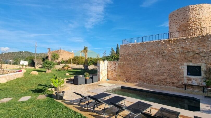 Finca Felanitx: Rustikaler Steinturm mit Pool, Sonnenliegen und gepflegtem Garten unter blauem Himmel.