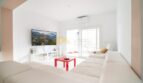Helles Wohnzimmer mit weißen Sofas, rotem Couchtisch, Flat-TV und Balkonzugang in modernisierter Wohnung in Arenal