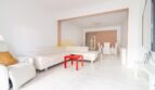 Helles Wohnzimmer mit weißen Ledersofas, rotem Couchtisch und offenem Durchgang zum Essbereich in modernisierter Wohnung in Arenal