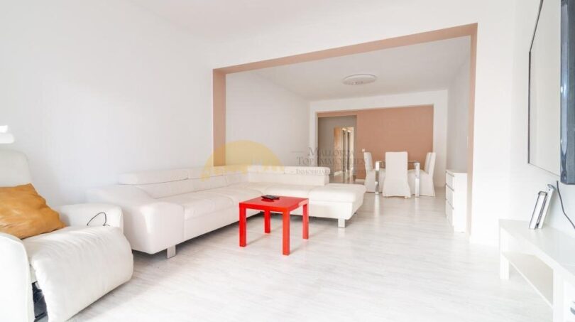 Helles Wohnzimmer mit weißen Ledersofas, rotem Couchtisch und offenem Durchgang zum Essbereich in modernisierter Wohnung in Arenal