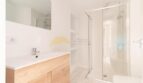 Modernes Badezimmer der Wohnung in Arenal mit Holzwaschtisch, Glasdusche und weißen Fliesen.