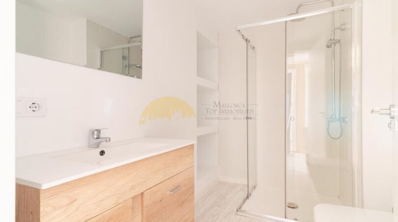 Modernes Badezimmer der Wohnung in Arenal mit Holzwaschtisch, Glasdusche und weißen Fliesen.