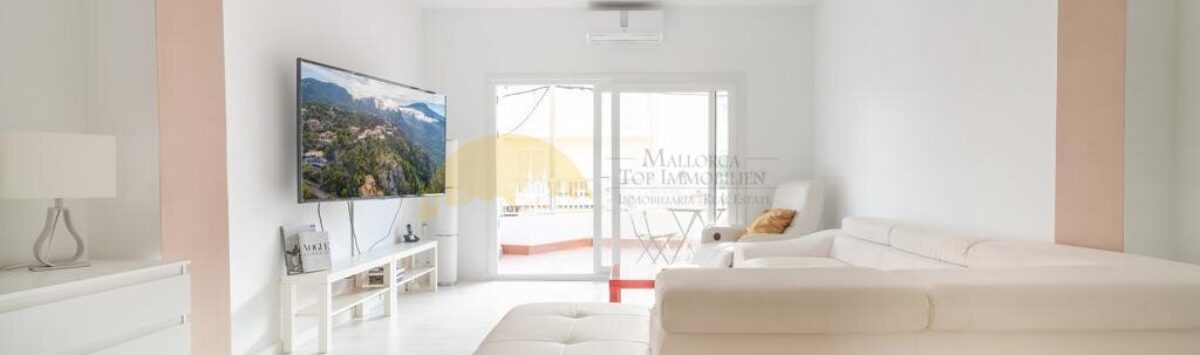 Helles Wohnzimmer mit weißem Ledersofa, TV und Zugang zur Terrasse in modernisierter Wohnung in Arenal