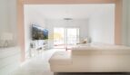Helles Wohnzimmer mit weißem Ledersofa, TV und Zugang zur Terrasse in modernisierter Wohnung in Arenal