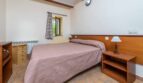 Schlafzimmer der Finca Son Macià mit Doppelbett, Holzmöbeln, Terrakottaboden und rustikalen Holzbalken.