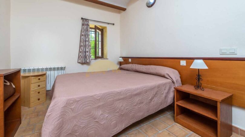 Schlafzimmer der Finca Son Macià mit Doppelbett, Holzmöbeln, Terrakottaboden und rustikalen Holzbalken.