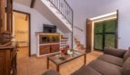 Wohnzimmer der Finca in Son Macià mit Treppe, Holzmöbeln, Flachbildschirm und grünen Fensterläden.