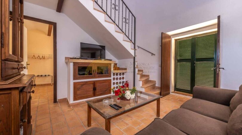 Wohnzimmer der Finca in Son Macià mit Treppe, Holzmöbeln, Flachbildschirm und grünen Fensterläden.