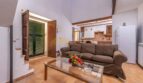 Wohnzimmer der Finca in Son Macià mit braunem Sofa, Glastisch, Holzbalken und offener Küche