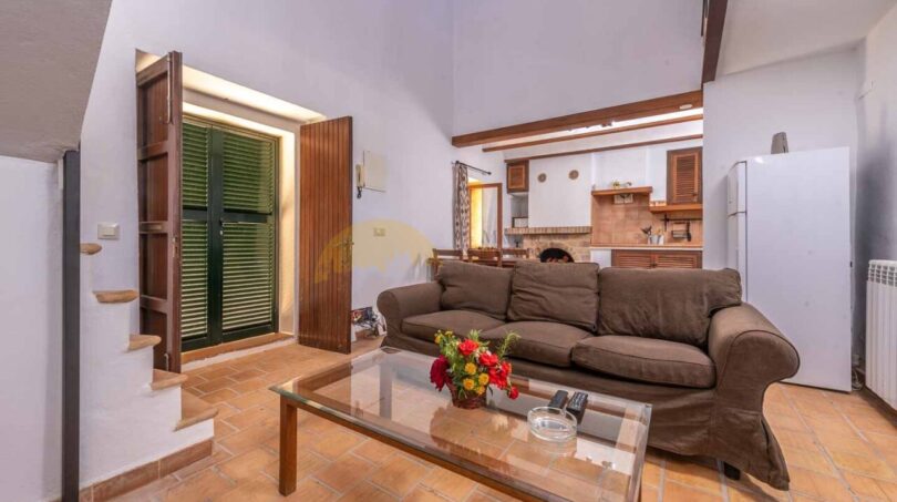 Wohnzimmer der Finca in Son Macià mit braunem Sofa, Glastisch, Holzbalken und offener Küche