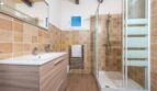 Modernes Badezimmer der Finca in Son Macià mit Glasdusche, Holzwaschtisch und warmen Terrakottafliesen.