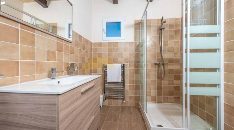 Modernes Badezimmer der Finca in Son Macià mit Glasdusche, Holzwaschtisch und warmen Terrakottafliesen.