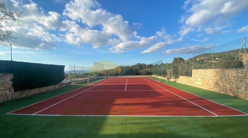 Roter Tennisplatz mit grünem Kunstrasen, Steinmauern und Panoramablick auf die Hügel von Son Macià