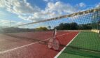 Tennisplatz der Finca in Son Macià mit rotem Belag, Netz und Schläger unter blauem Himmel