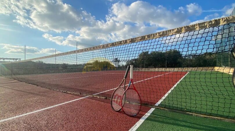 Tennisplatz der Finca in Son Macià mit rotem Belag, Netz und Schläger unter blauem Himmel