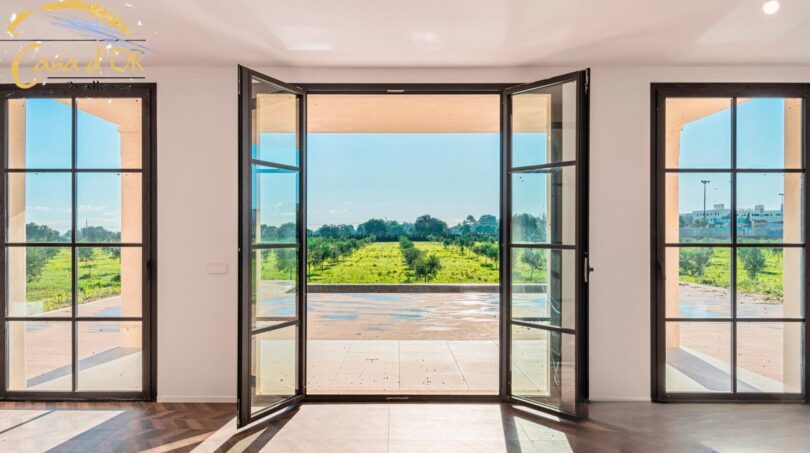Großzügige Glastüren öffnen sich zur Terrasse mit Blick auf grüne Olivenhaine beim Neubau-Landhaus Porto Cristo