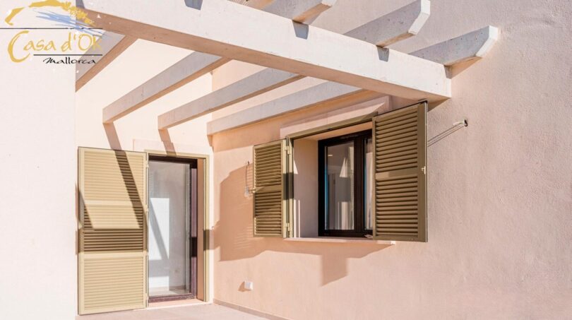 Terrasse des Neubau-Landhauses in Porto Cristo mit Holzpergola und grünen Fensterläden
