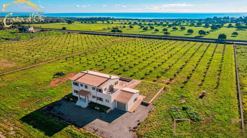 Luftaufnahme eines weißen Neubau-Landhauses bei Porto Cristo, umgeben von Feldern mit Meerblick.