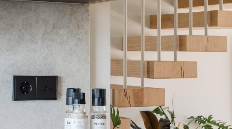 Moderne Küche der Maisonette mit Holzschränken, Gewürzmühlen und schwebender Designtreppe